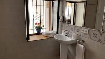 Een badkamer met een wastafel, spiegel en raam met uitzicht op een balkon.