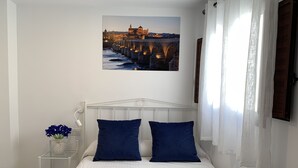 Ein ordentlich eingerichtetes Schlafzimmer mit einem Bett, Kissen, einem Nachttisch mit Lampe, einem Wandbild und einem Fenster mit Vorhängen.