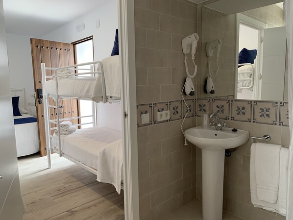 Habitación de hotel con literas, baño con lavamanos y espejo, y zona de ducha.