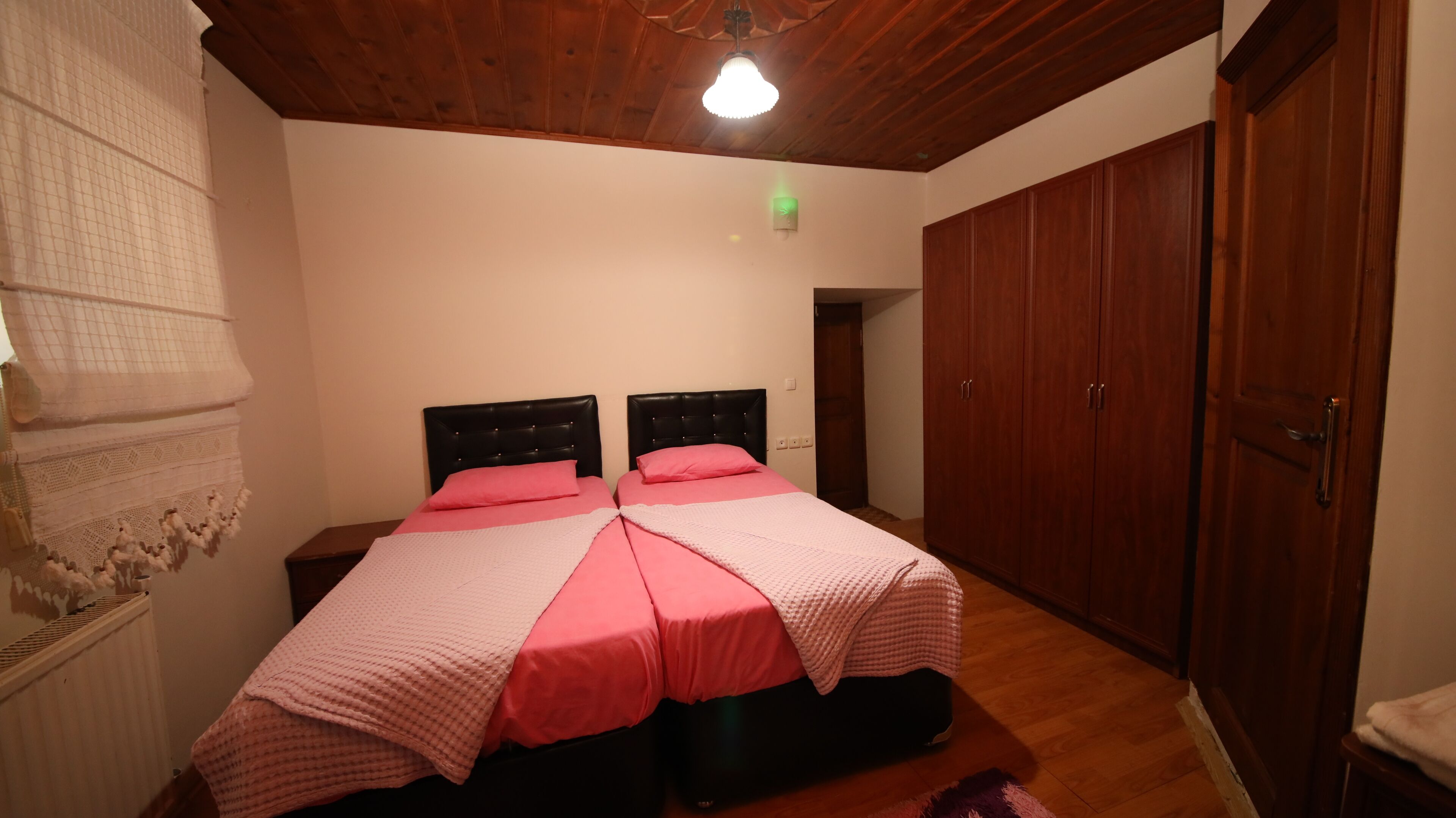 A bedroom with two beds, wooden wardrobe, and a ceiling light.