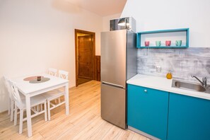 A compact kitchen with a white table and chairs, a stainless steel refrigerator, and a blue countertop with a sink. - Apartament przy Walach Chrobrego (Szczecin)