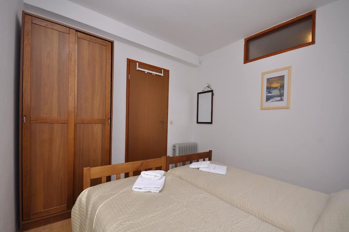A bedroom with a bed, a wooden wardrobe, a radiator, and a framed picture on the wall.