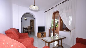 A living room with red sofas, a television on a wooden stand, and a dining area with chairs and a table. - Apartments Margareta (Pula)