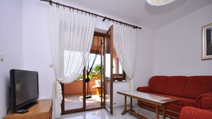 A room with a TV on a wooden stand, a red sofa, a small table, and a glass door leading outside. - Apartments Margareta (Pula)