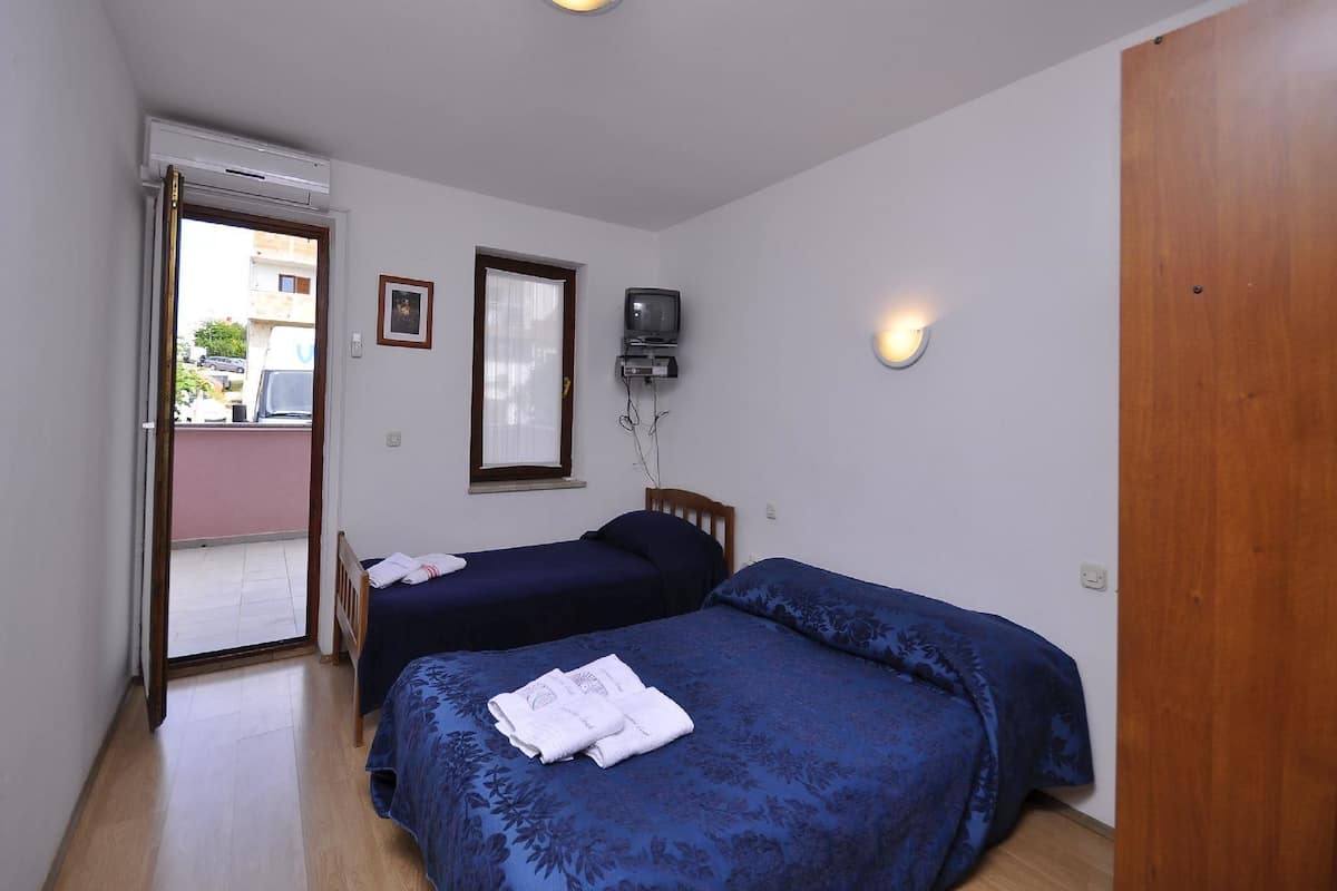 A bedroom with two beds, a TV, a ceiling fan, and a sliding door leading to an outdoor area.