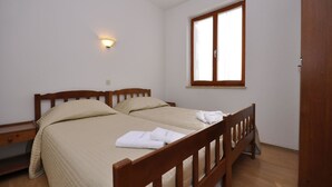 A single bed with a wooden frame, a bedside table, a wall-mounted light, and a window with blinds. - Apartments Margareta (Pula)