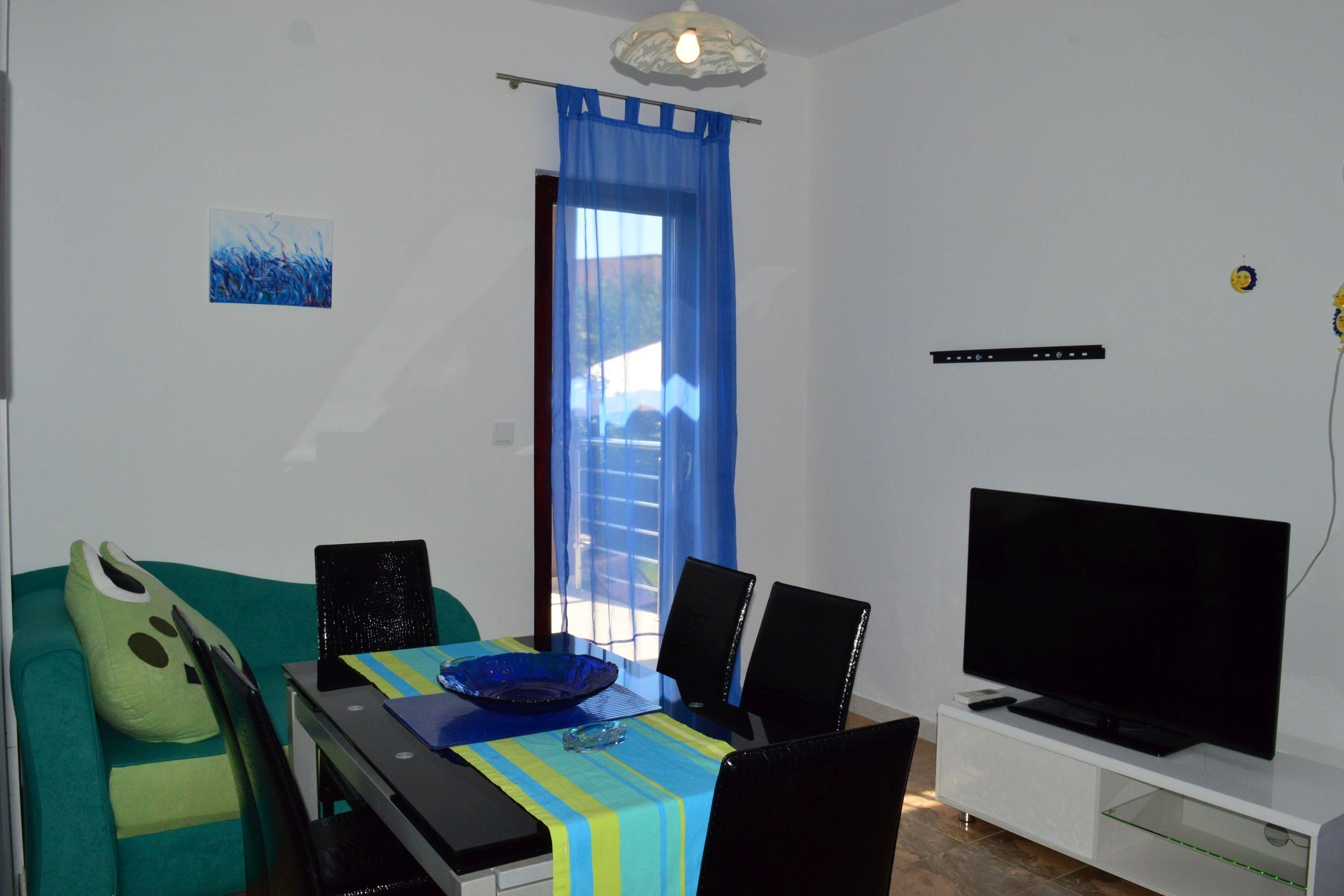 A compact living space with a dining area, a sofa, a television, and a window with blue curtains.
