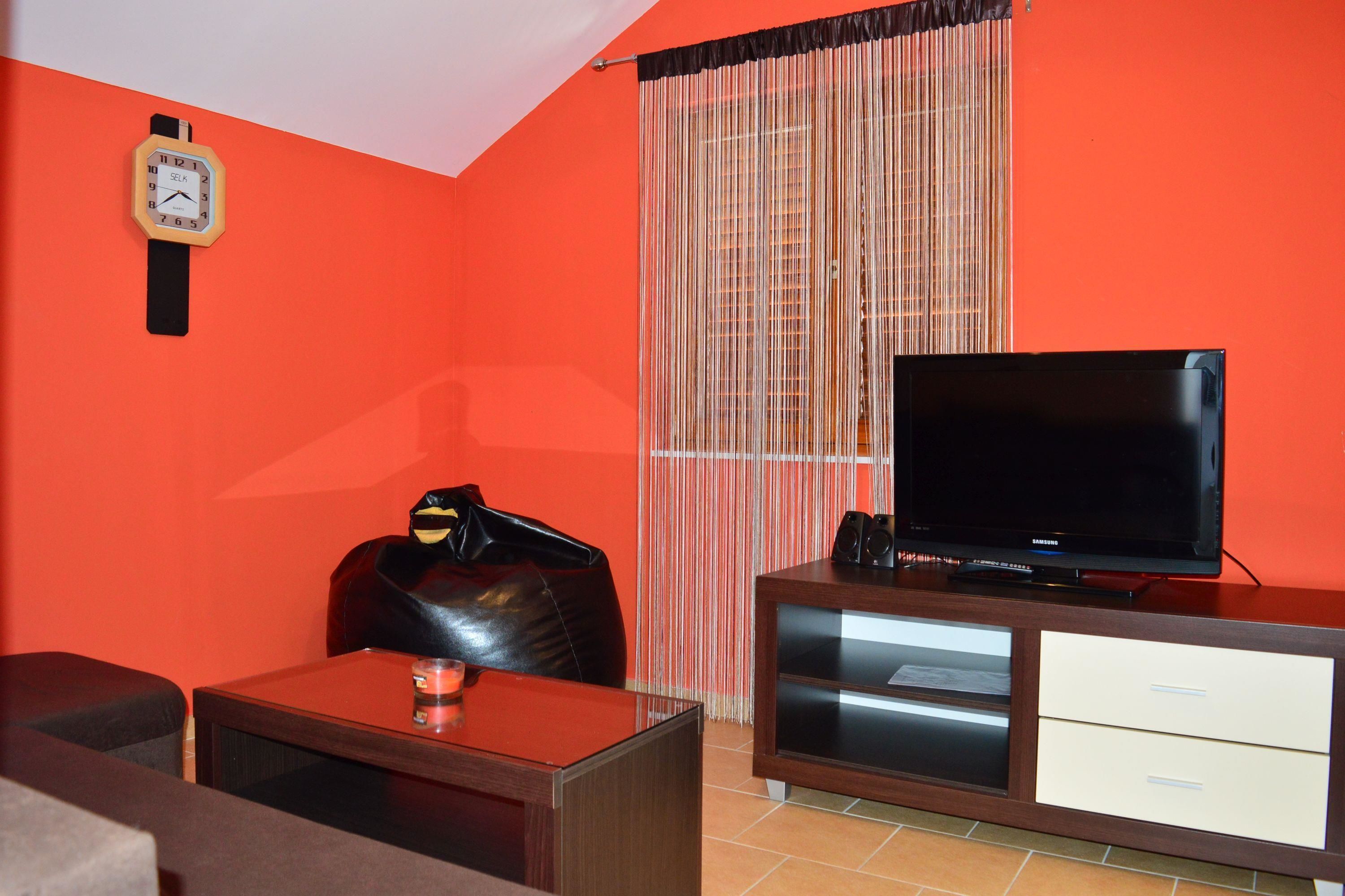 A living room with a television, a clock, and a leather chair.