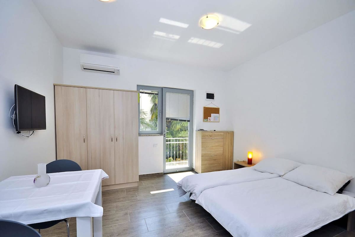 A bedroom with a bed, a desk, a chair, a wardrobe, and a television.