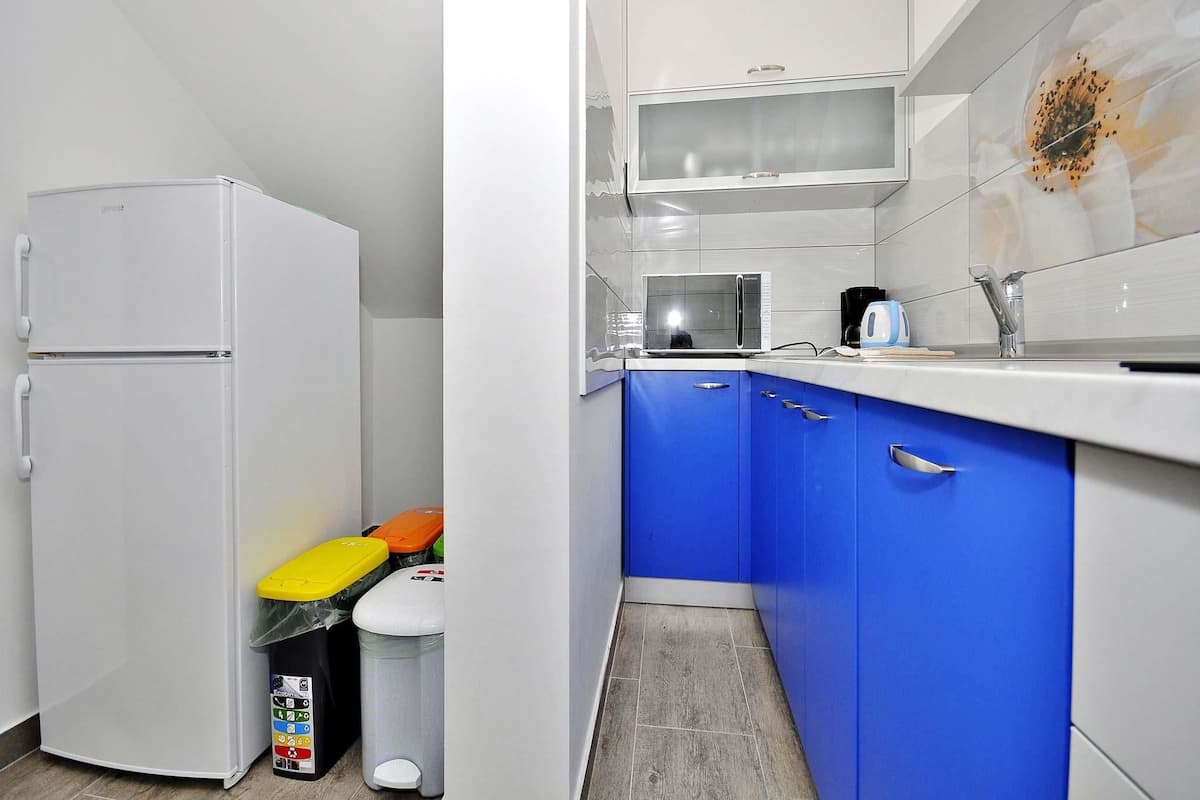 A compact kitchen with white cabinets, a microwave, and a sink. There are trash bins and a small refrigerator.