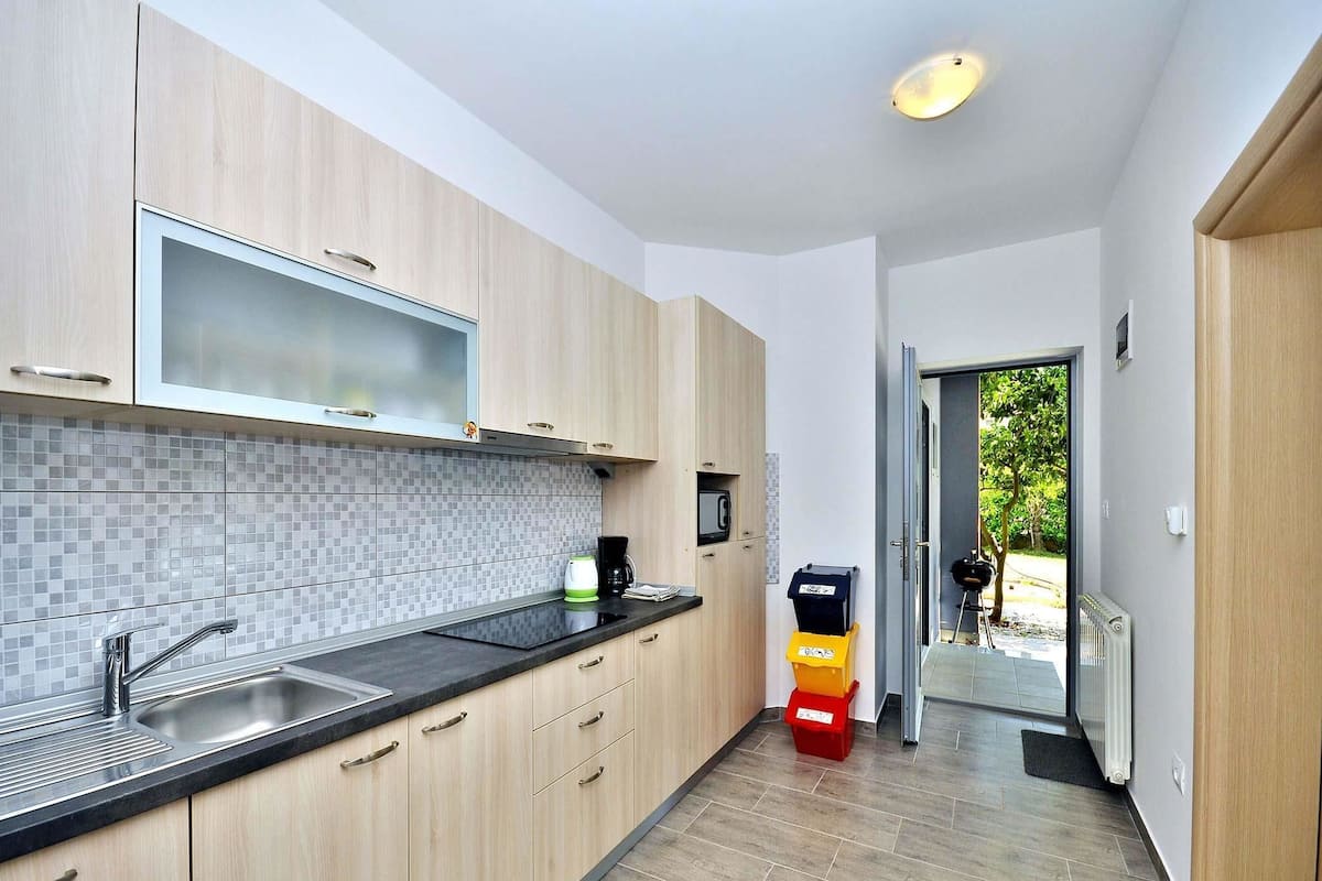 A modern kitchen with light wood cabinets, a black countertop, and a tiled backsplash.