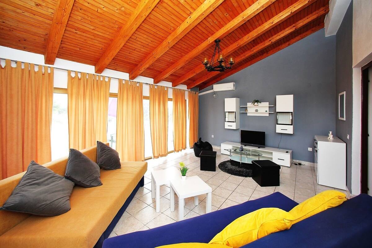 A modern living room with a wooden ceiling, a sofa, a coffee table, a TV, and a kitchen area with a fridge and microwave.