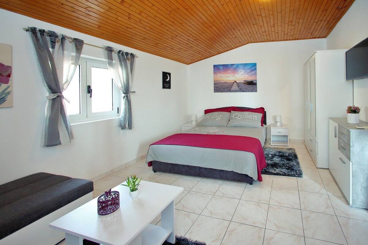 A bedroom with a bed, a desk, a chair, a TV, and a window with curtains.