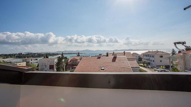 A residential area with red-tiled roofs, a clear sky, and a distant view of the sea and mountains. - Apartments Adria (Zadar)