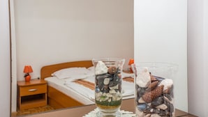 A room with a bed, a nightstand with a lamp, and two glass vases with decorative stones. - Apartments Adria (Zadar)
