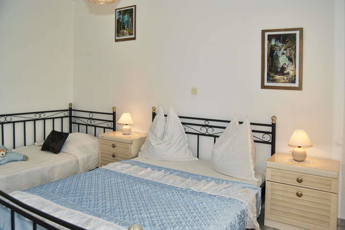 A bedroom with two single beds, bedside tables with lamps, and two framed pictures on the wall.