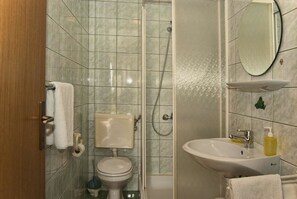 Un baño con inodoro, ducha, lavamanos y espejo.