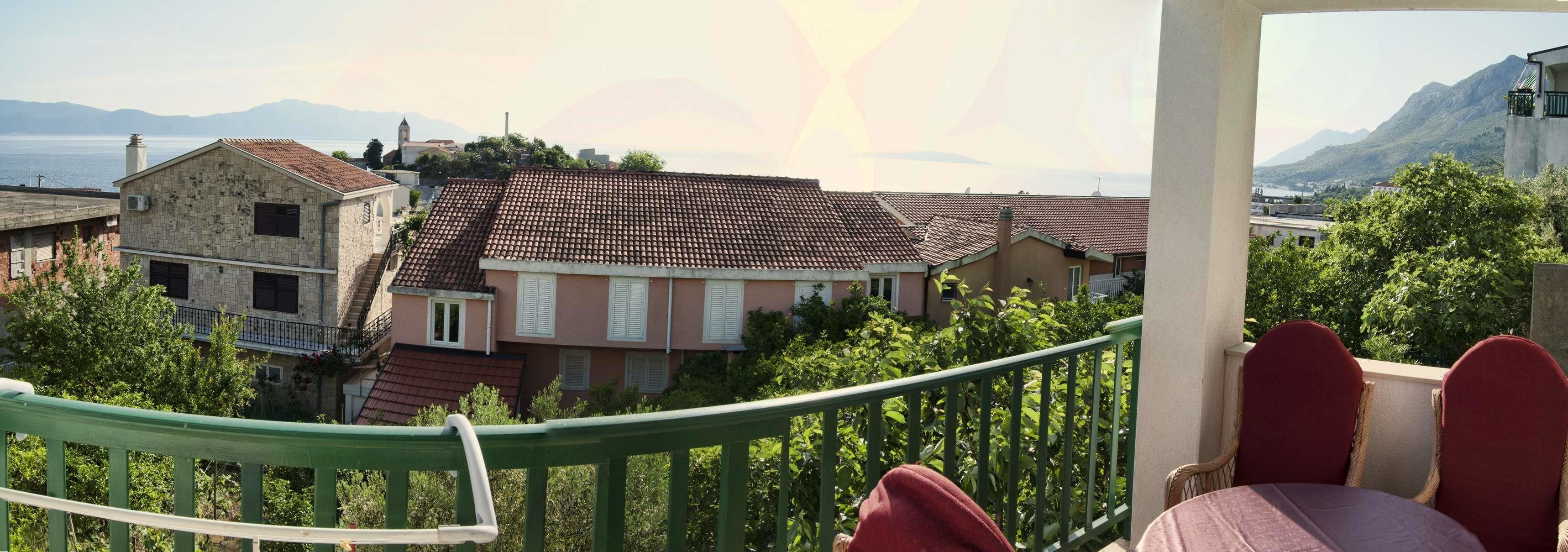 Un balcon offrant une vue sur une ville côtière, des bâtiments en pierre et une montagne en arrière-plan.