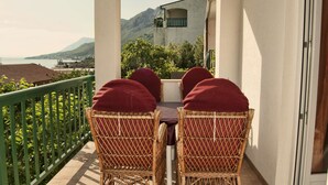 A balcony with wicker chairs and a table, overlooking a mountainous landscape and a body of water.