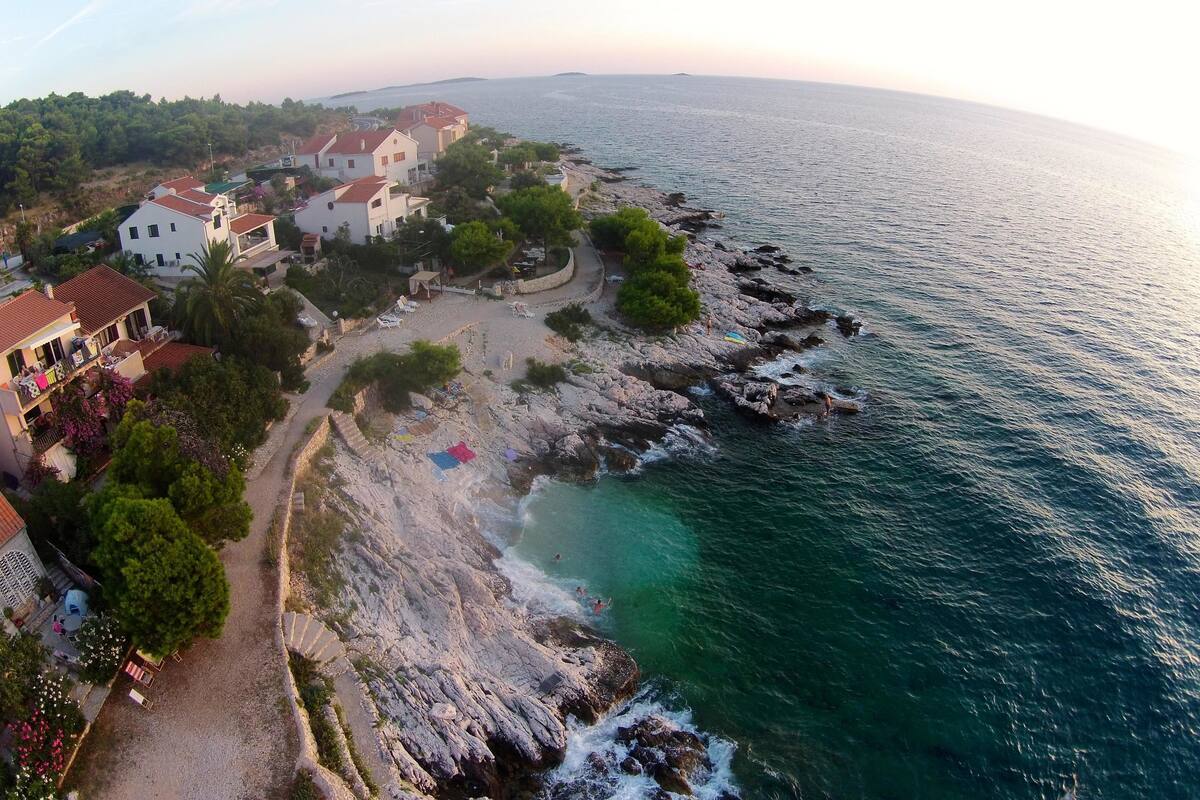 Une propriété située sur la côte, avec une plage rocheuse, une vue dégagée sur la mer et plusieurs maisons dotées de balcons.