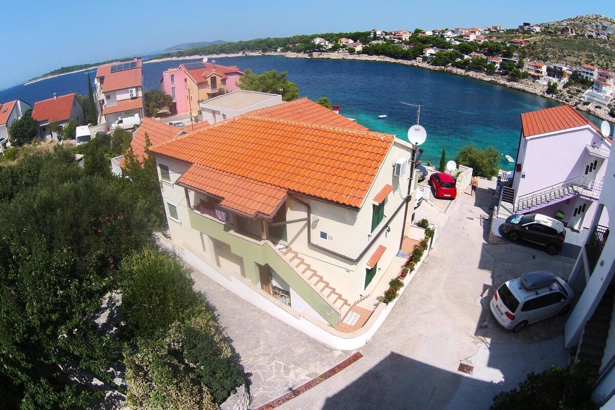 Un bâtiment situé sur la côte, avec un toit recouvert de tuiles rouges, une antenne parabolique et une voiture garée devant.