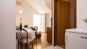A compact kitchen with a refrigerator, a dining area with a table and chairs, and a small potted plant. - Apartments Skarpa (Rogoznica)