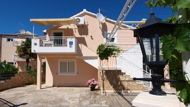 A residential building with a balcony, satellite dish, and a small garden with pink flowers. - Apartments Skarpa (Rogoznica)