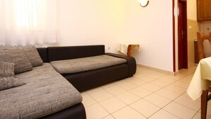 A living room with a sofa, a small table, and a kitchen area visible through an open door. - Apartments Skarpa (Rogoznica)