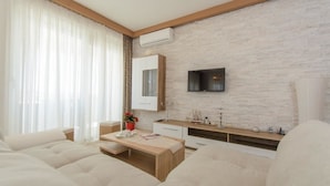 A modern living room with a sofa, a wooden coffee table, a TV mounted on a brick wall, and a small decorative ship model. - Apartments Villa Aurora 3 (Okrug)