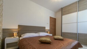 A bedroom with a large bed, two bedside lamps, a wooden headboard, and a sliding door. - Apartments Villa Aurora 3 (Okrug)
