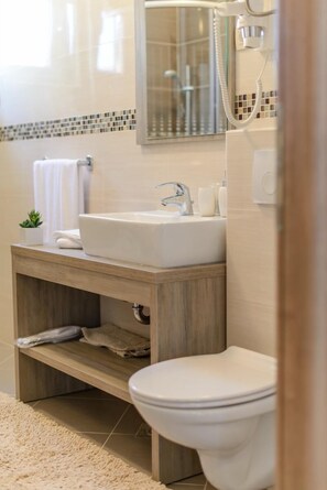 A modern bathroom with a white sink, a toilet, and a shower area. - Apartments Villa Aurora 3 (Okrug)