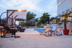 An outdoor pool area with a lounge chair, a wicker chair, and a table. - Apartments Villa Aurora 3 (Okrug)