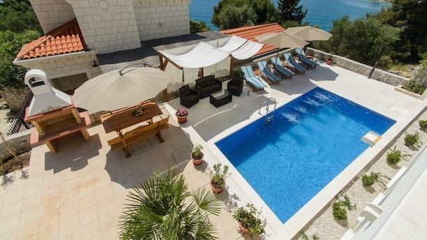 A pool area with a view of the sea, outdoor seating, and a small building with a tiled roof. - Apartments Villa Aurora 3 (Okrug)