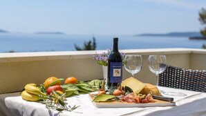 A table with a bottle of Peliasac wine, a plate of food, and two glasses on a balcony overlooking a body of water. - Apartments Villa Aurora 3 (Okrug)