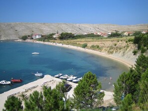 A coastal area with boats docked, a sandy beach, and buildings in the background. - Apartments Komadina M73 (Pag)