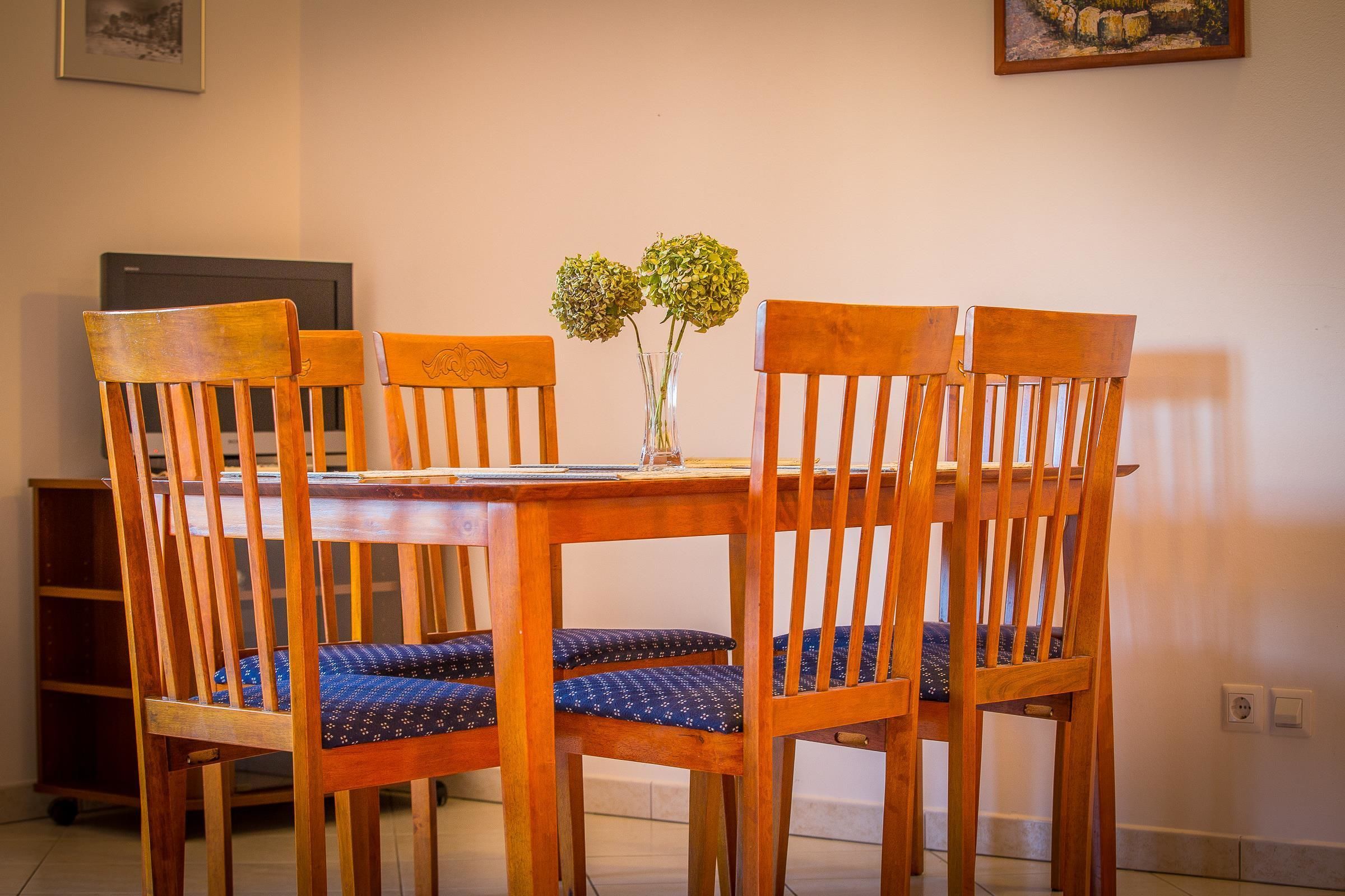 A dining table with four wooden chairs, a vase with flowers, and a painting on the wall.