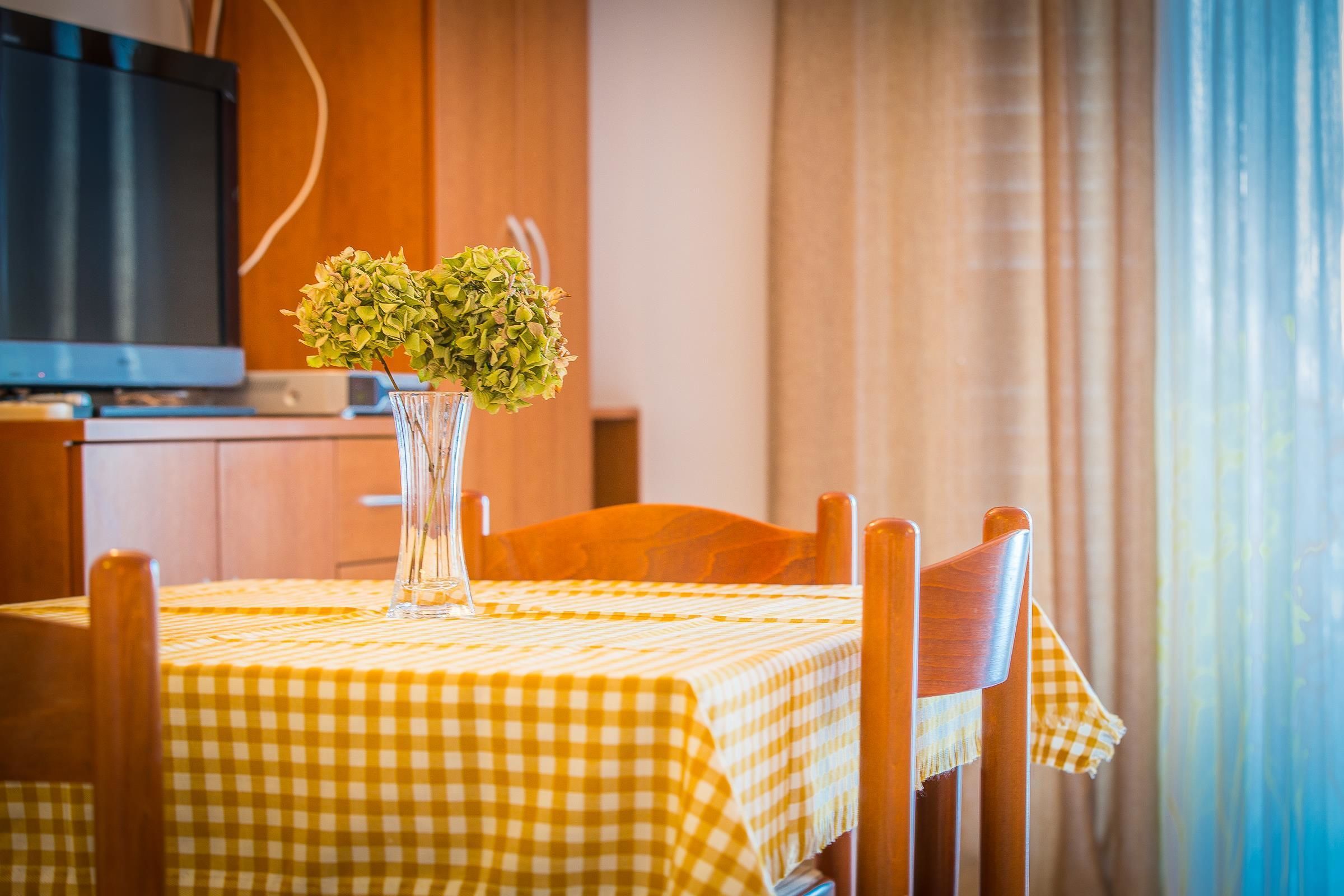 Una mesa de comedor con mantel a cuadros amarillo, un florero con follaje verde y sillas de madera.