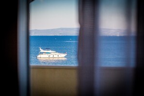 A view of a calm sea with a boat and distant land through a window.
