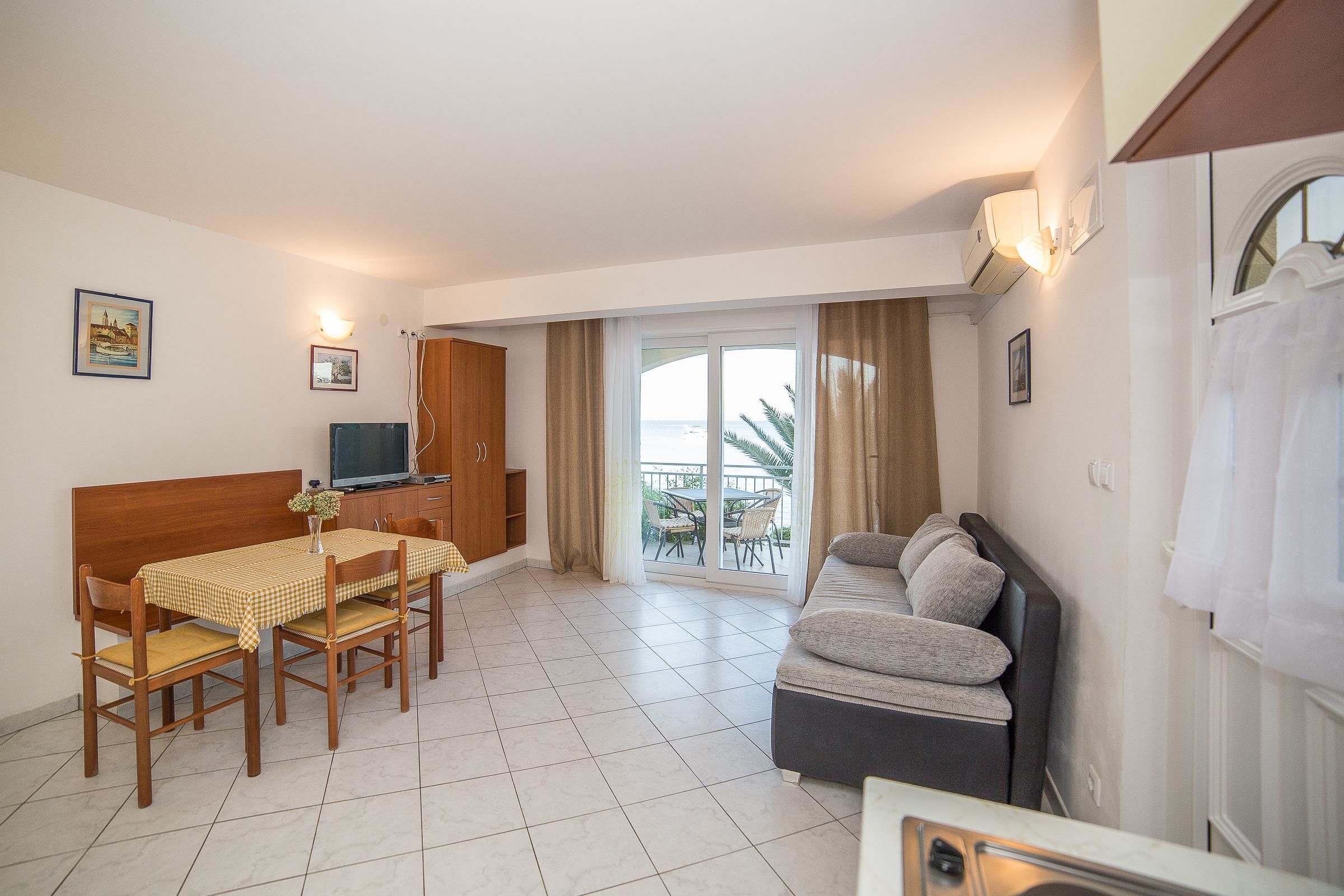 A compact living space with a dining area, a sofa, a TV, and a balcony with a view.