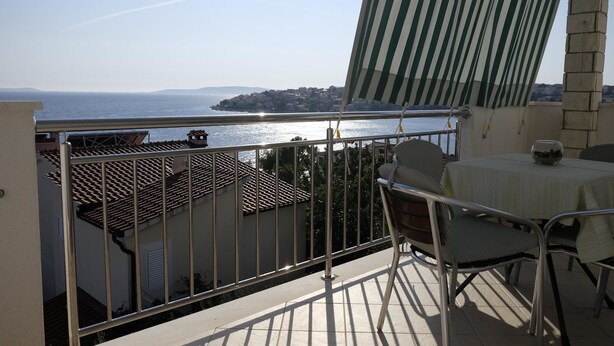 A balcony with a view of the sea, a table with a bowl, and metal chairs.