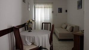 A dining area with a round table, chairs, and a vase of flowers. There is a sofa and a small table with a bowl on it.