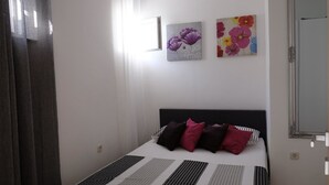 A bedroom with a bed, two wall-mounted paintings, a window with curtains, and a mirror.