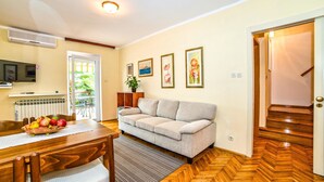 A living room with a sofa, a dining table with chairs, a fruit basket, and a television. - Apartments Paliaga (Rovinj)