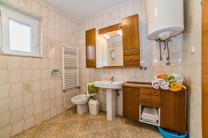 A bathroom with a pedestal sink, a mirror, a toilet, and a bidet. There is a window and a towel rack with towels. - Apartments Paliaga (Rovinj)