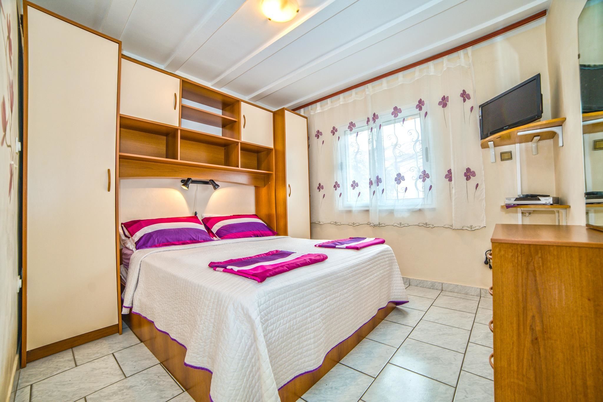 A bedroom with a bed, built-in wardrobe, and a television on a stand.