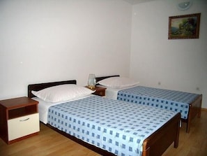 A bedroom with two single beds, wooden headboards, a nightstand with a lamp, and a small drawer unit.