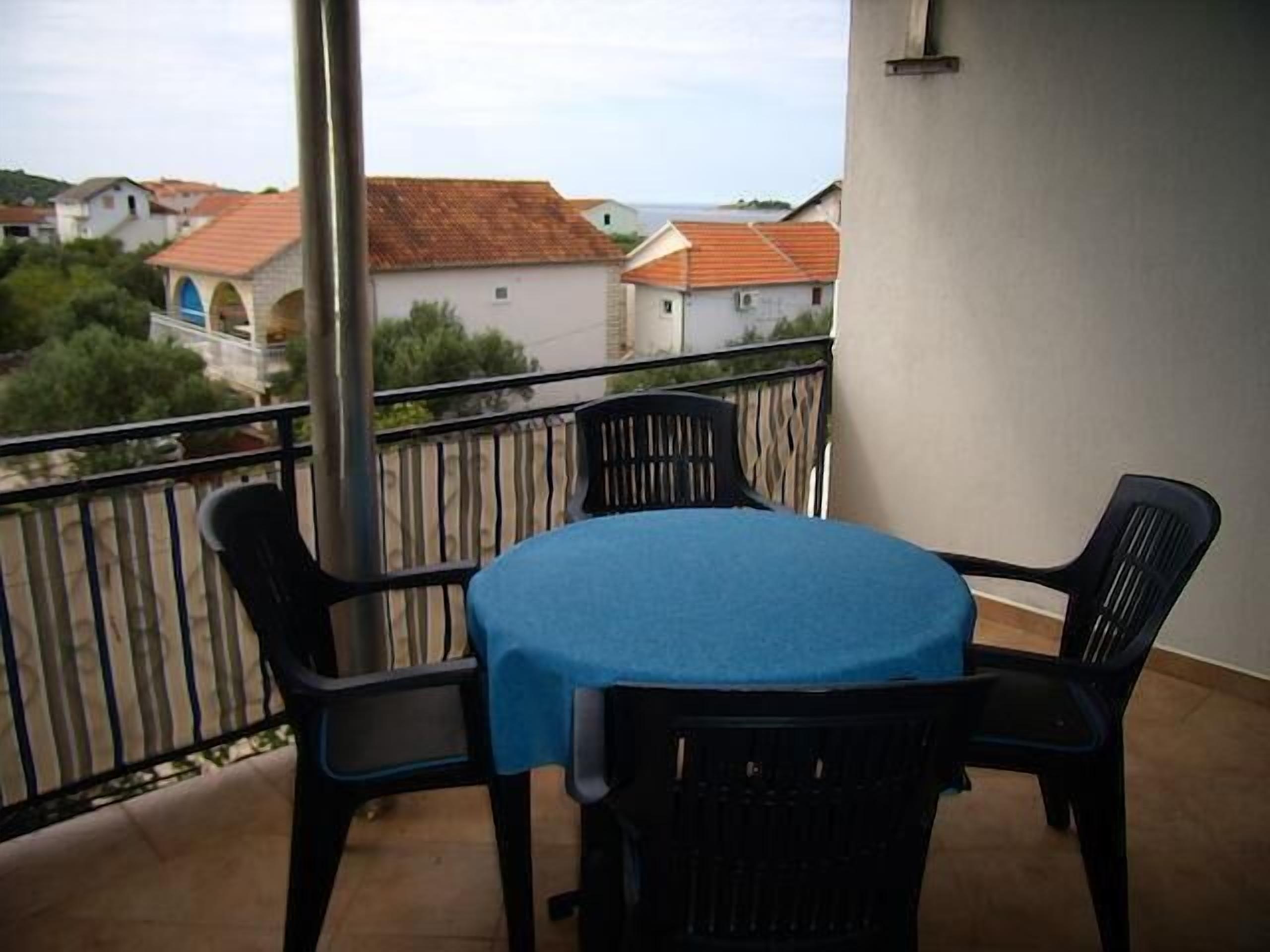 A balcony with a table and chairs, overlooking a residential area with houses and a body of water.