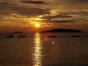 A sunset over a calm sea with boats and a distant island.