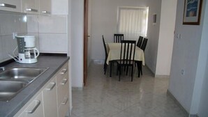 A kitchen with a coffee maker, a dining table with chairs, and a window with curtains. - Apartments Ivan Rogoznica (Rogoznica)