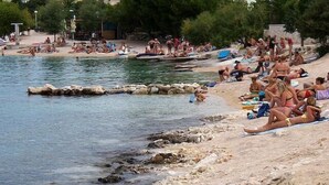 A beach with people sunbathing and swimming, surrounded by buildings and trees. - Apartments Ivan Rogoznica (Rogoznica)